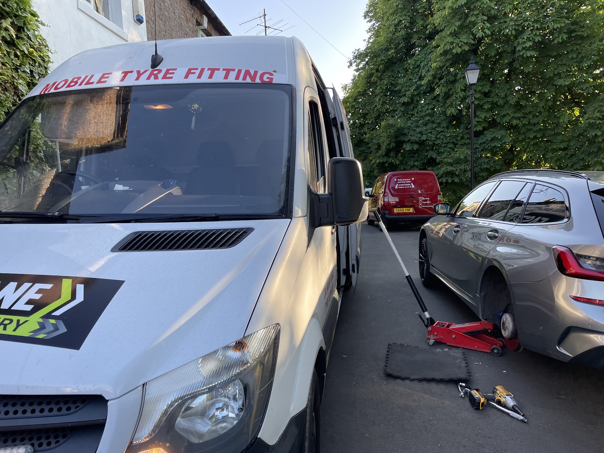 A mobile tyre fitting van parked beside a car on a jack in a residential street